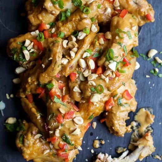 A pile of Thai peanut chicken wings on a black surface with one wing eaten down to the bone