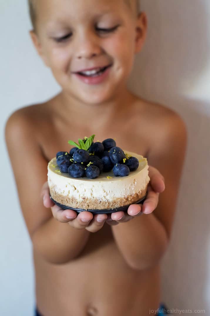 A child holding a Mini Goat Cheese Cheesecake topped with blueberries