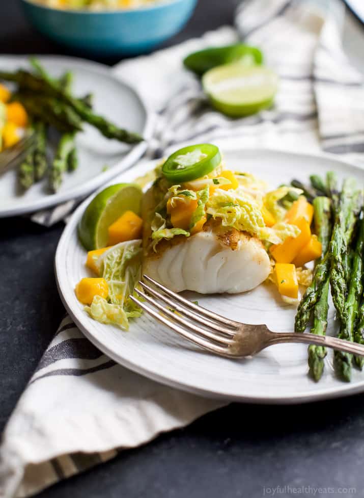 Grilled White Fish topped Mango Jalapeno Coleslaw next to asparagus on a plate