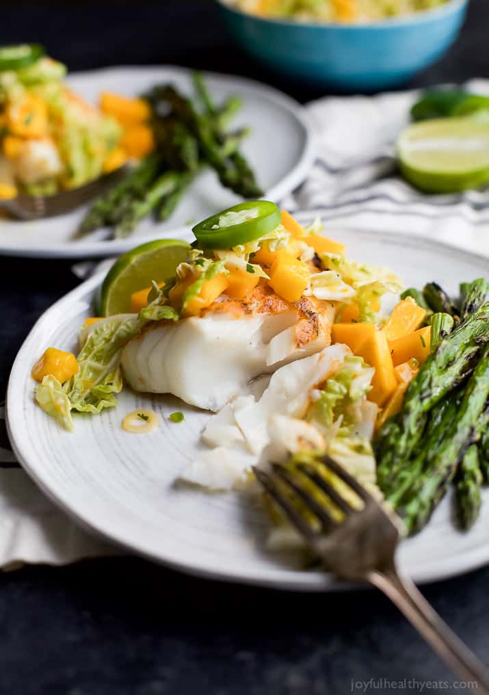 Grilled White Fish topped with Mango Jalapeno Coleslaw next to asparagus on a plate
