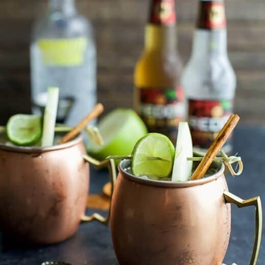 Apple cider mules in copper glasses garnished with cinnamon sticks, apple slices, and lime slices.