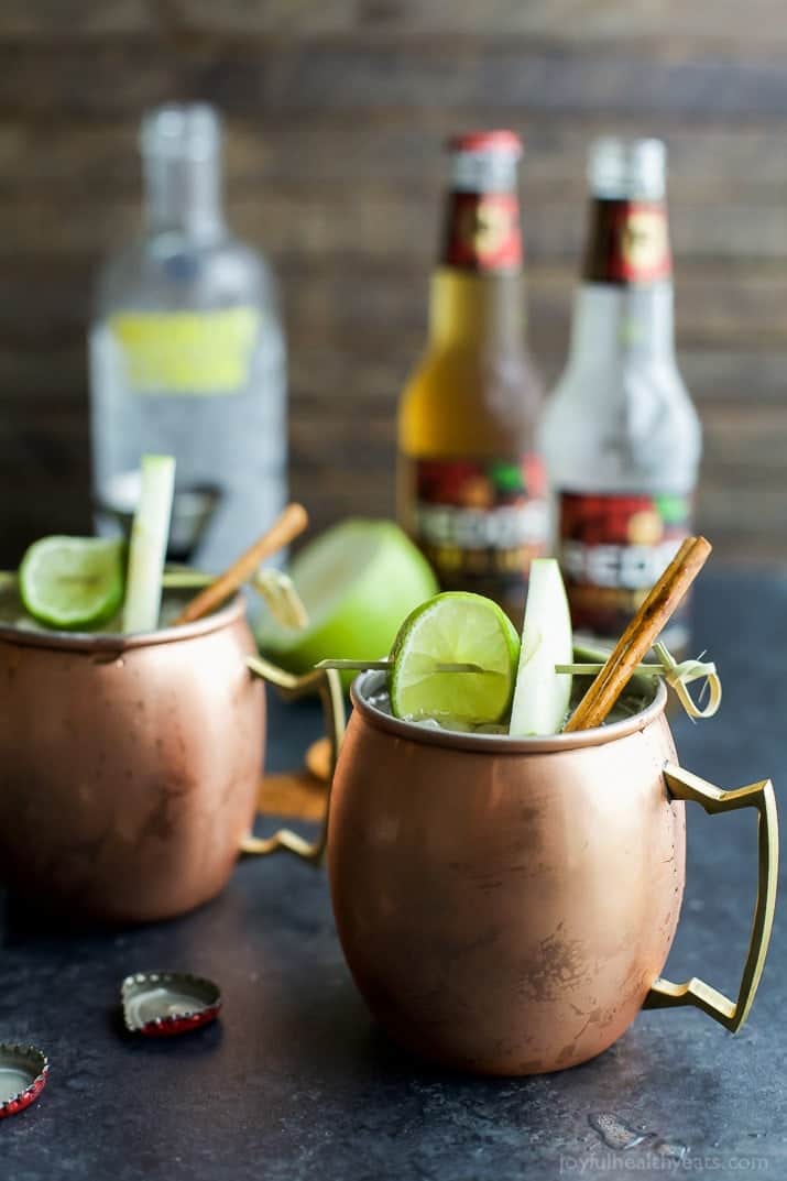 Apple cider mules in copper glasses garnished with cinnamon sticks, apple slices, and lime slices.