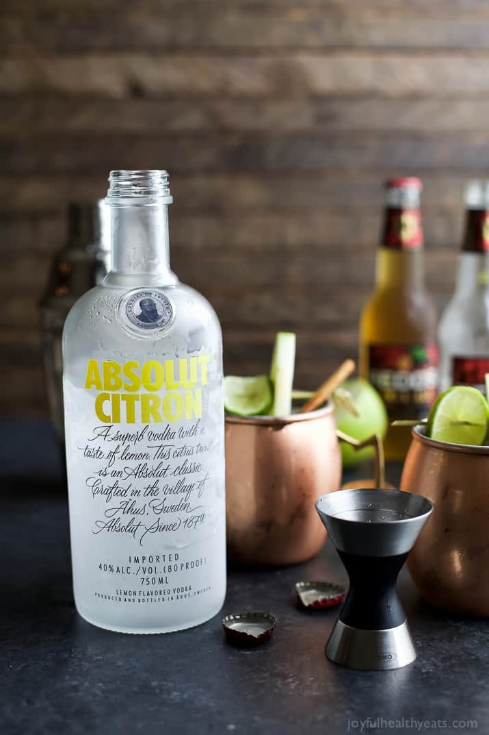 A bottle of Absolut Citron next to copper mugs of apple cider moscow mules