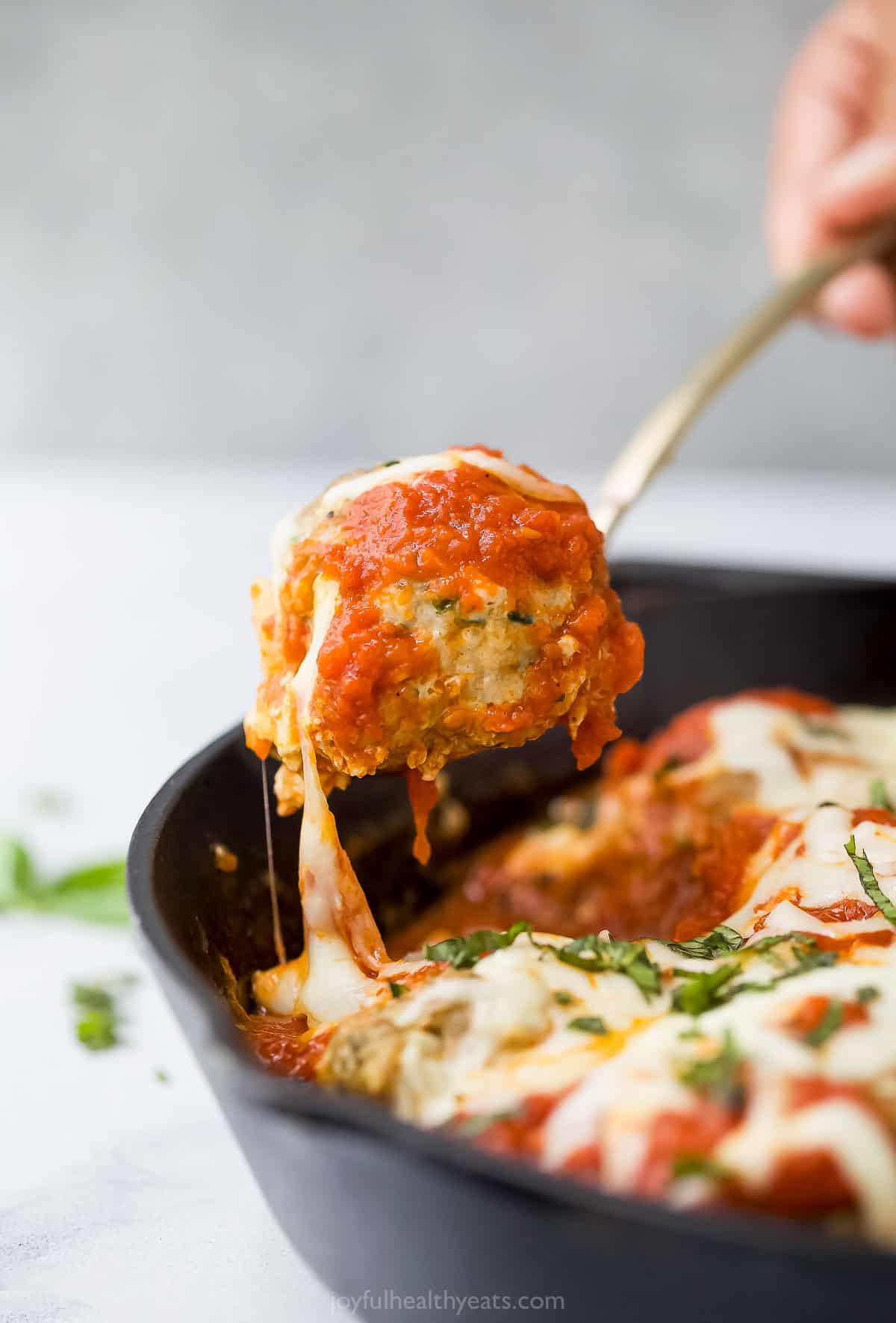 These Baked Turkey Meatballs are cooked in marinara to keep them flavorful and moist, and they’re also loaded with cheese. Done in 30 minutes! Spoon lifting baked turkey meatball from pan
