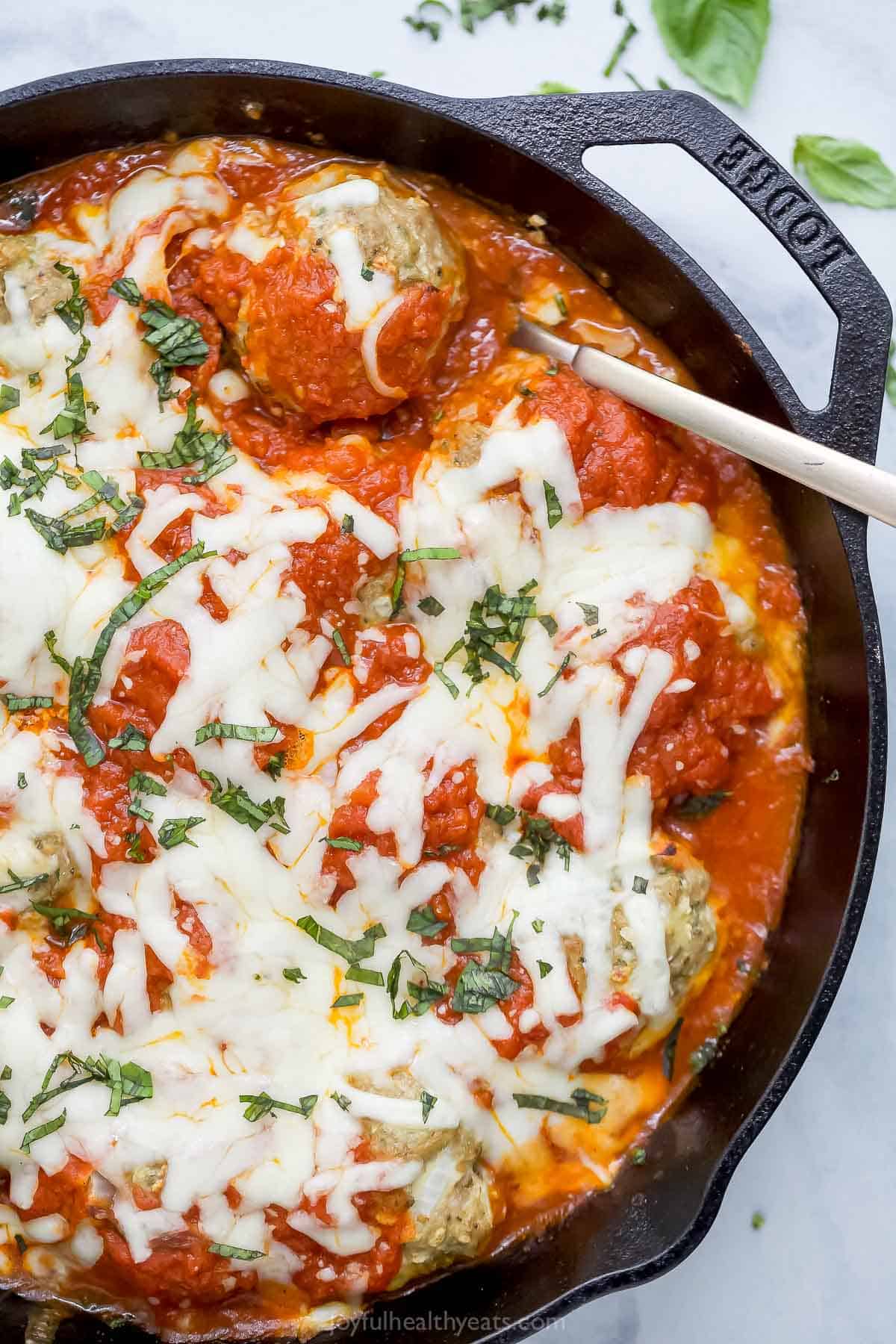 These Baked Turkey Meatballs are cooked in marinara to keep them flavorful and moist, and they’re also loaded with cheese. Done in 30 minutes! Overhead view of baked turkey meatballs in cast iron skillet with marinara and mozzarella