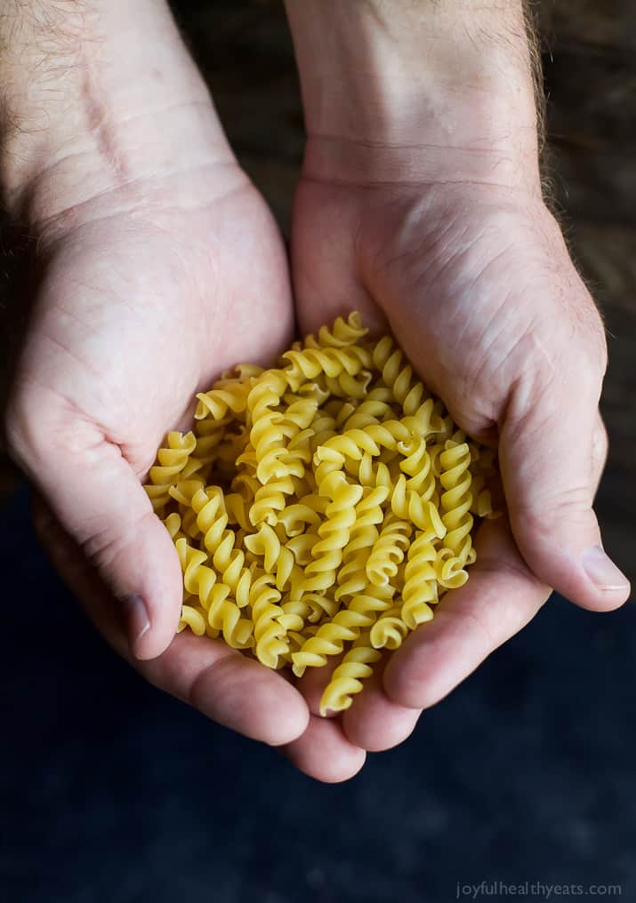 Two hands holding dry rotini pasta