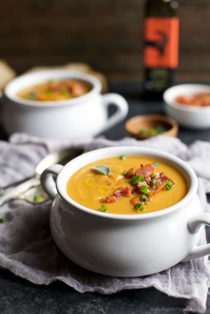 A crock of Creamy Bacon Roasted Butternut Squash Soup garnished with bacon and scallions