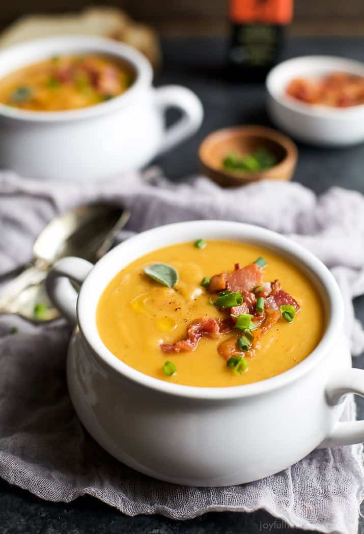 A crock of Creamy Bacon Roasted Butternut Squash Soup garnished with crumbled bacon and scallions