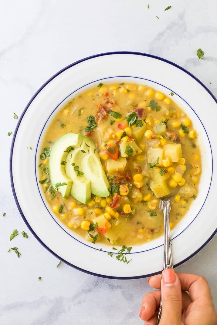 close up of a bowl filled with crock pot potato corn chowder topped with avocado