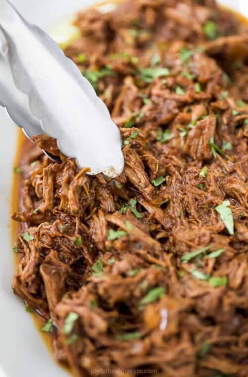 tongs picking up slow cooker barbacoa short rib tacos