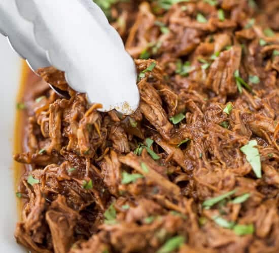 tongs picking up slow cooker barbacoa short rib tacos