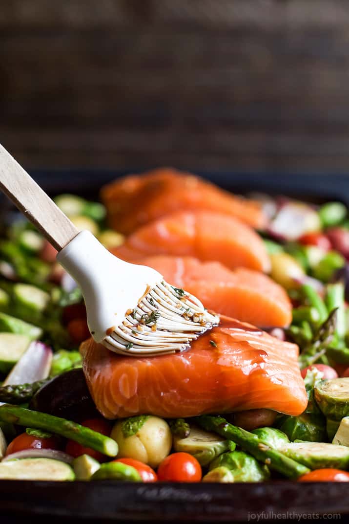 Sheet Pan Salmon on a bed of potatoes, asparagus, and brussels sprouts being brushed with balsamic