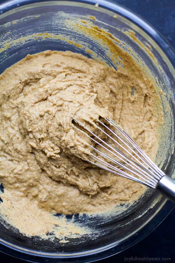 A glass bowl full of batter being mixed with a whisk.