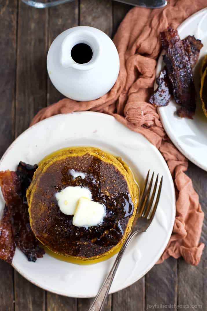 A plate of whole wheat pancakes beside a jar of pure maple syrup and a kitchen towel
