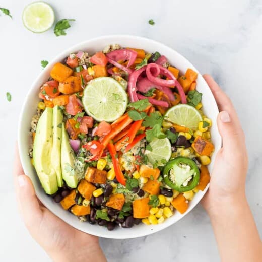 hands holding easy sweet potato black bean quinoa bowls with crema