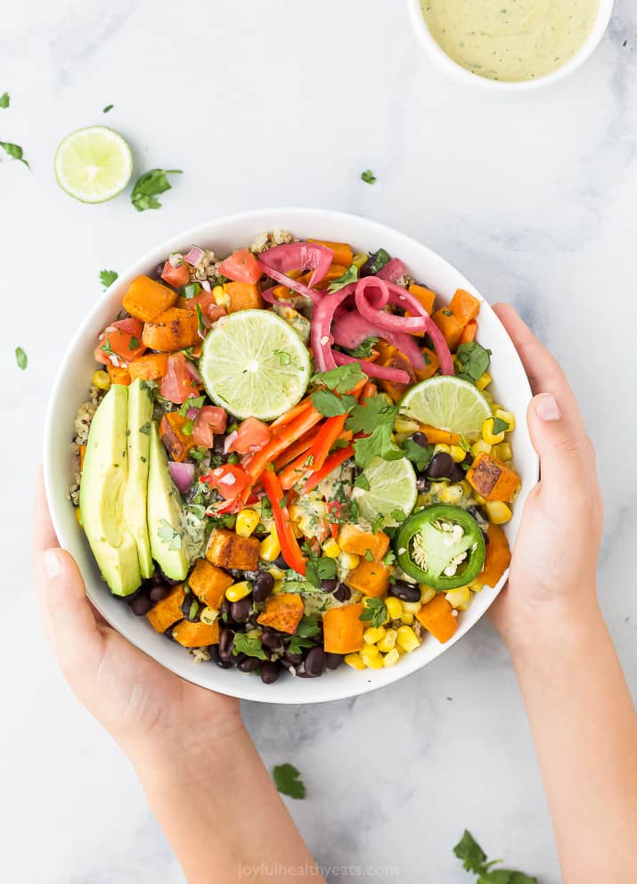 hands holding easy sweet potato black bean quinoa bowls with crema