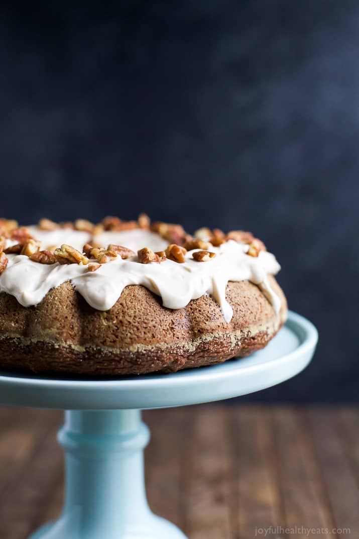 A pumpkin cake with cream cheese frosting on a tall cake stand with a black backdrop