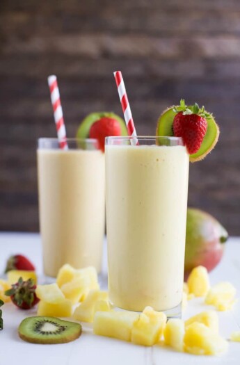 Two glasses of creamy Tropical Mango Smoothie served with pineapple, strawberries, kiwi, and a straw | joyfulhealthyeats.com | #drinkitallin #ad