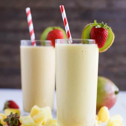 Two glasses of creamy Tropical Mango Smoothie served with pineapple, strawberries, kiwi, and a straw | joyfulhealthyeats.com | #drinkitallin #ad