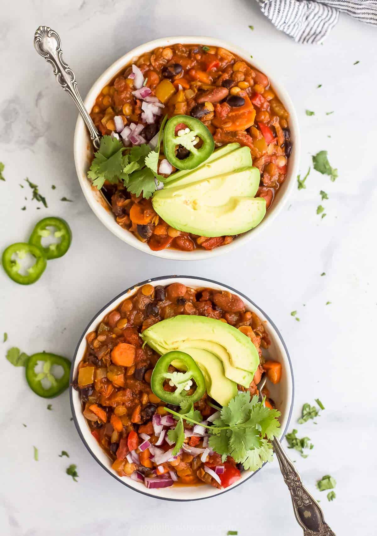 Two bowls filled with vegetarian lentil chili and toppings.