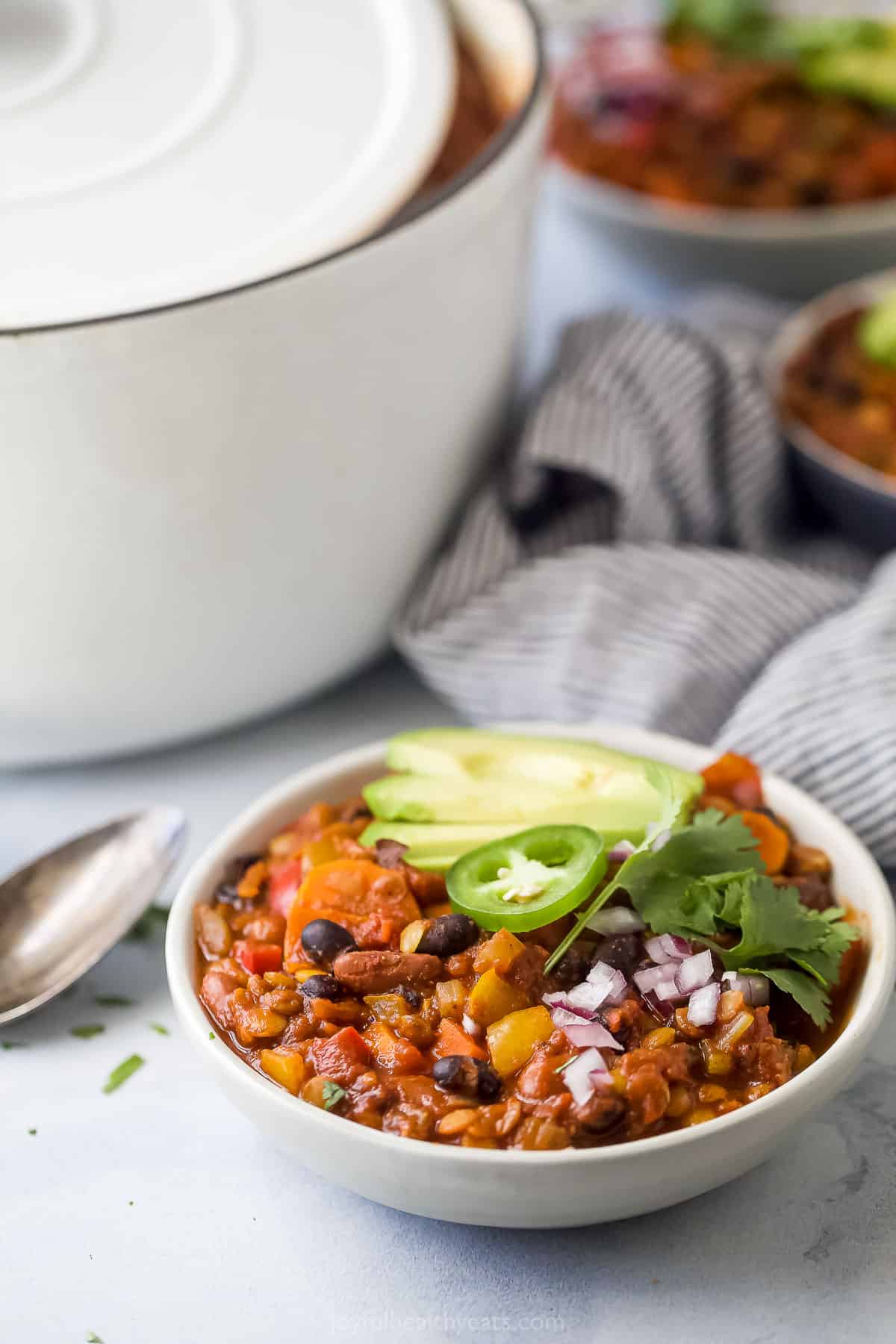 Lentil chili with toppings and a dutch oven in the background.