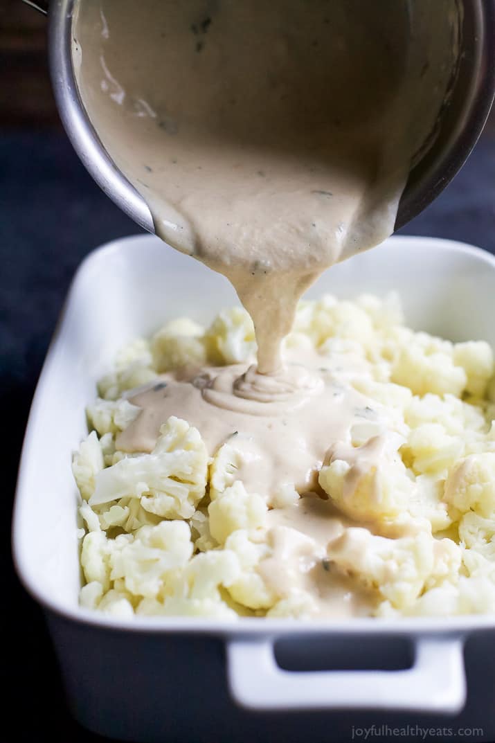 Cheddar sauce being poured over chopped cauliflower in a baking dish