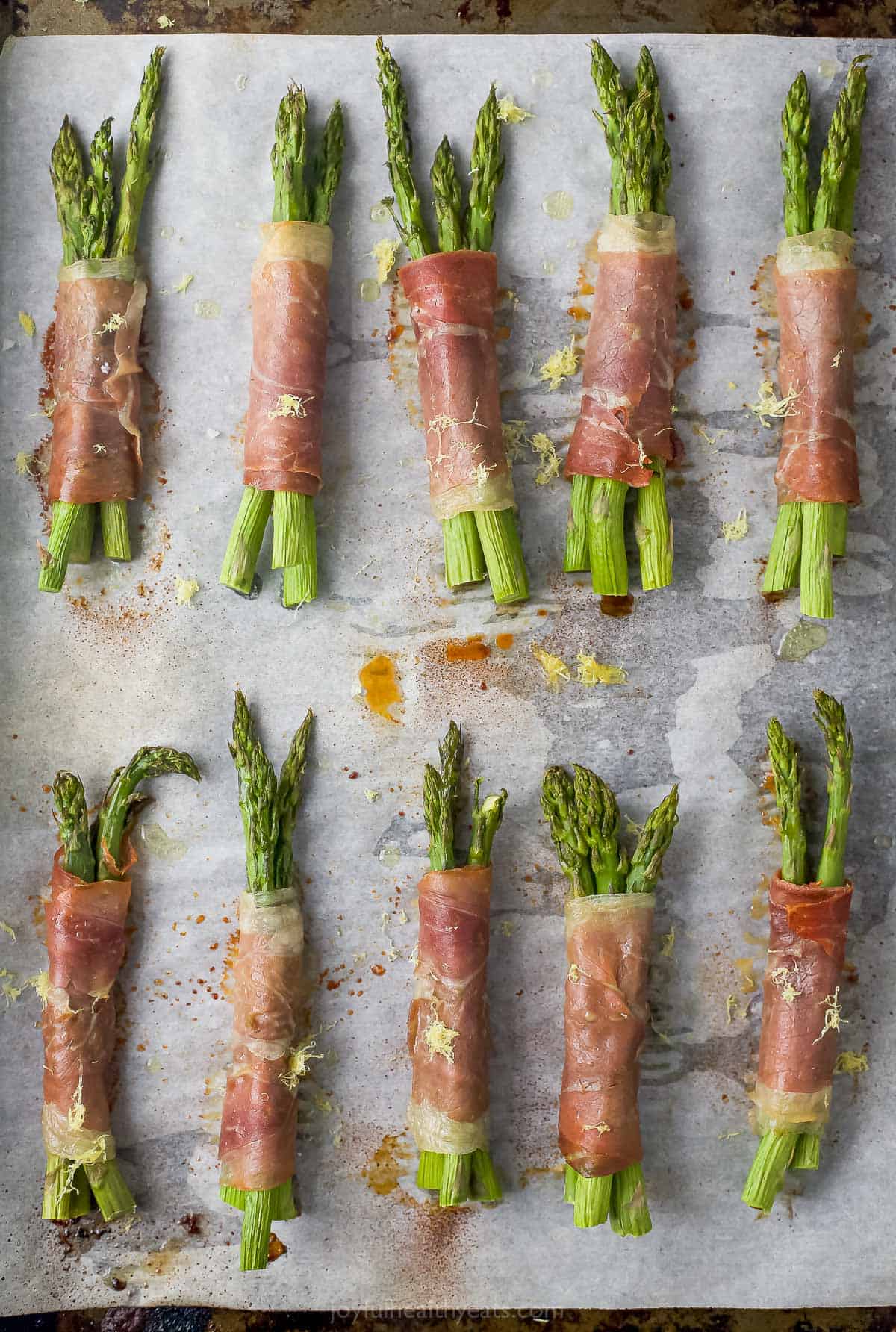 Ten baked asparagus bundles seasoned with salt on a baking sheet