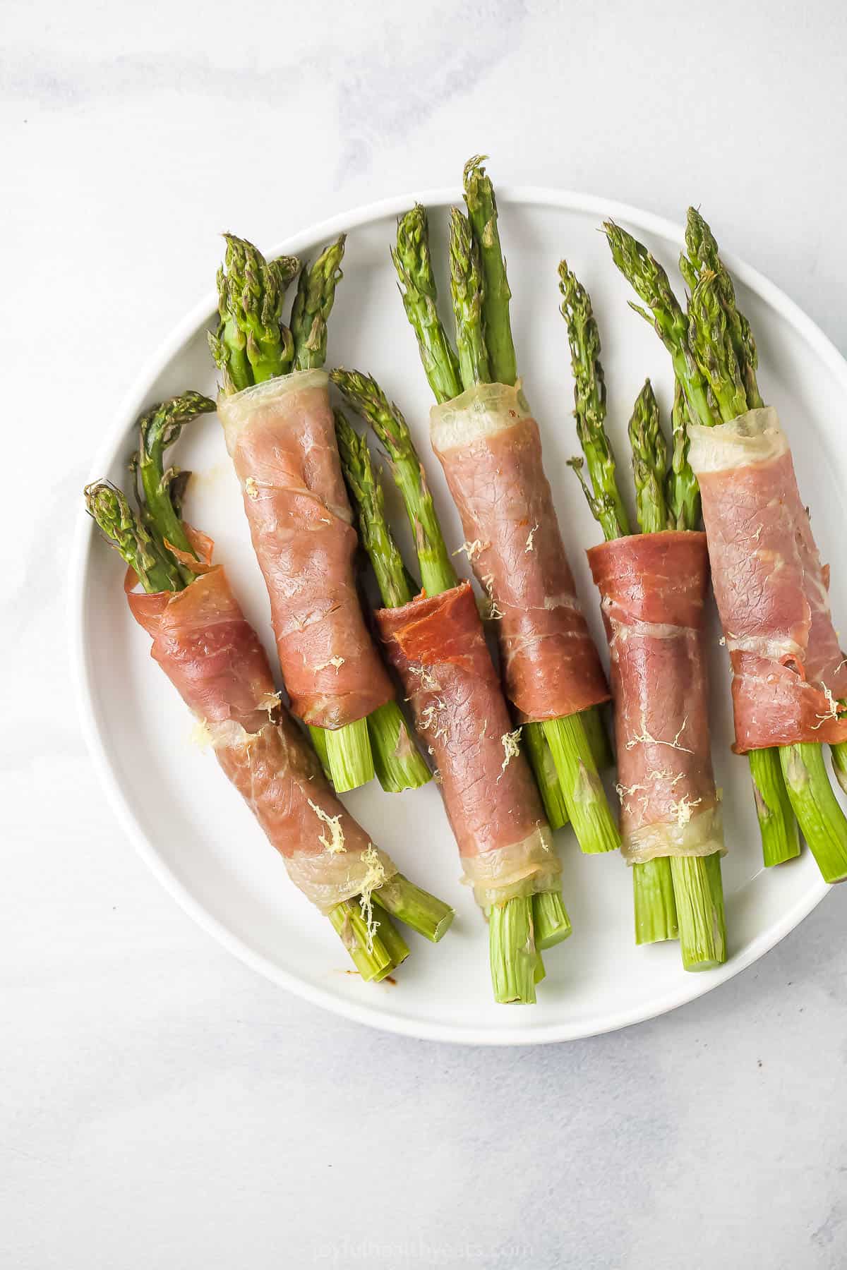 A plate full of prosciutto-wrapped asparagus on a marble kitchen countertop