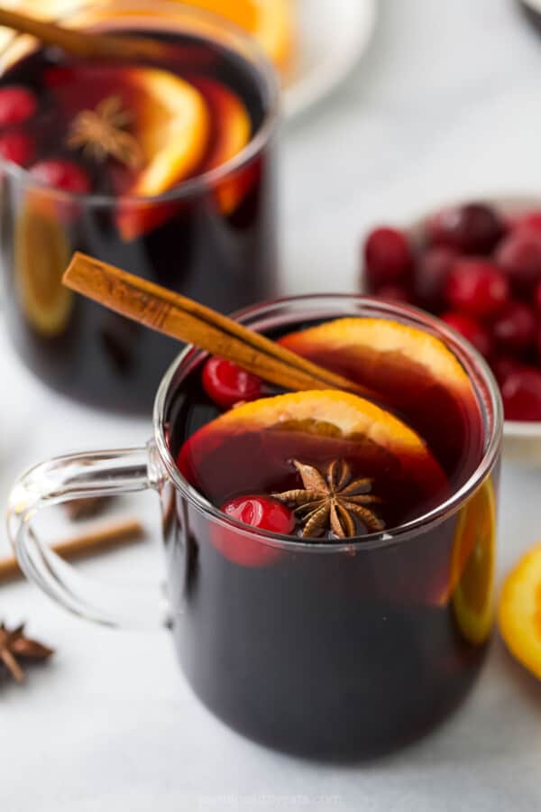 Glass of mulled wine recipe with orange slices and a cinnamon stick.