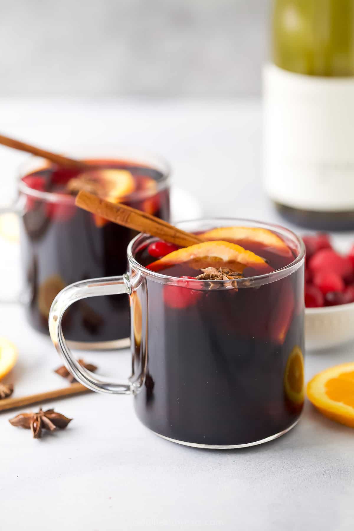 Warm holiday drink in a glass with sliced oranges and a cinnamon stick stirrer. 