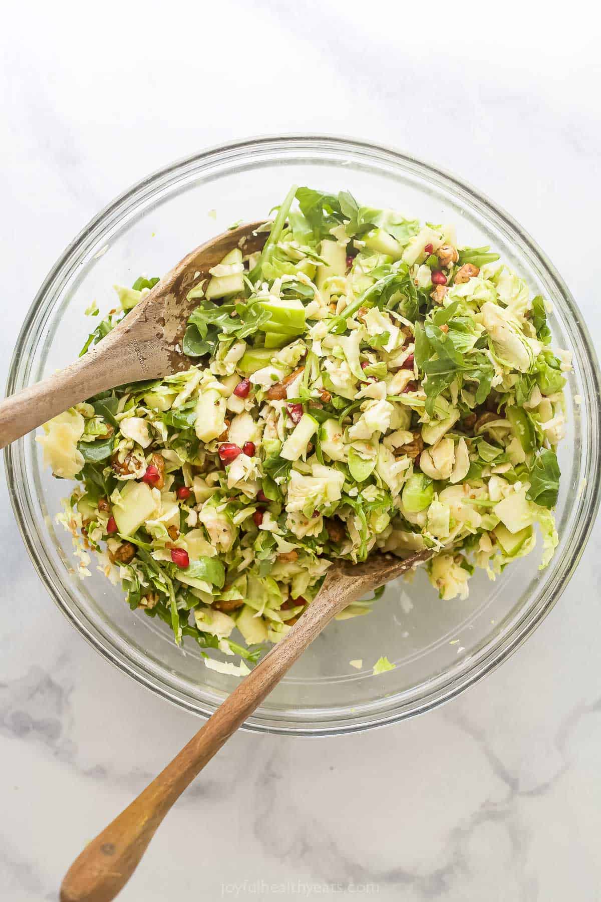 Deux cuillères en bois dans un bol à mélanger en verre avec la salade de choux de Bruxelles.