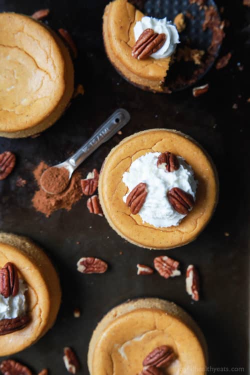 Five mini pumpkin pecan cakes on a baking sheet with a teaspoon of ground cinnamon