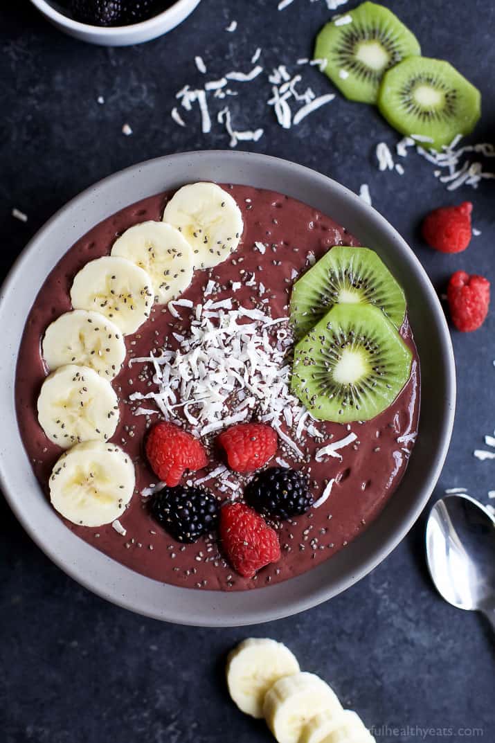 a dark red smoothie bowl with kiwi, banana slices, berries, and shredded coconut