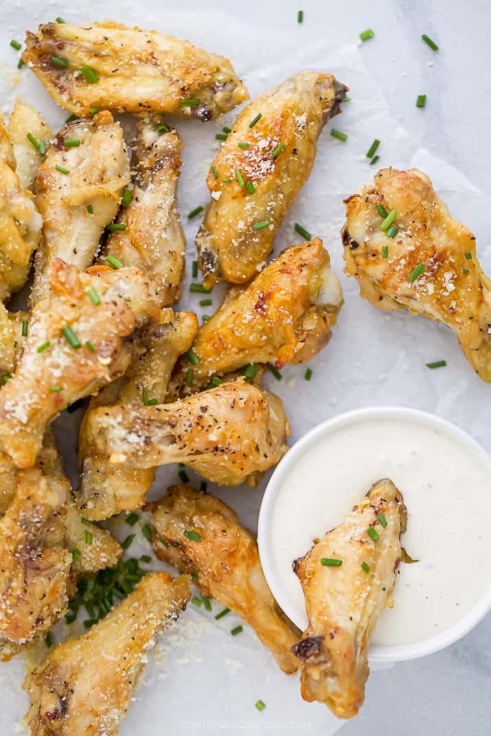 a pile of crispy baked garlic parmesan chicken wings with a cup of creamy dipping sauce