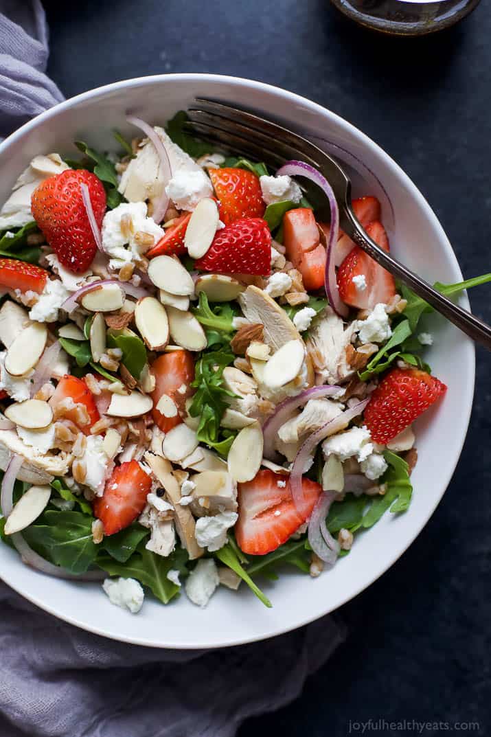 Top view of FARRO ARUGULA STRAWBERRY CHICKEN SALAD in a bowl with sliced almonds and goat cheese