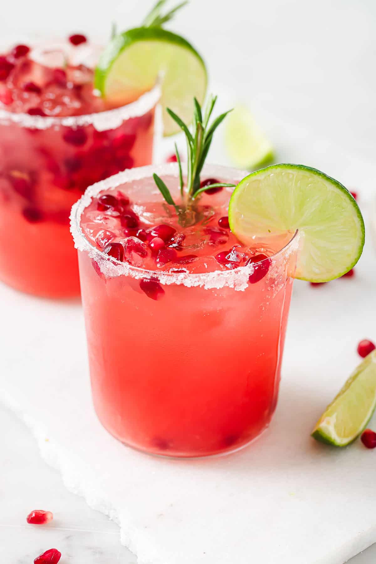 Pomegranate margarita with rosemary sprigs and lime wedges. 
