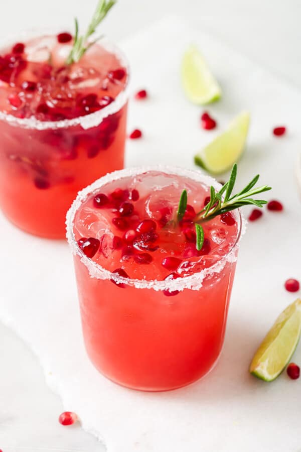 Tilted photo of pomegranate margarita with pomegranate seeds and rosemary.