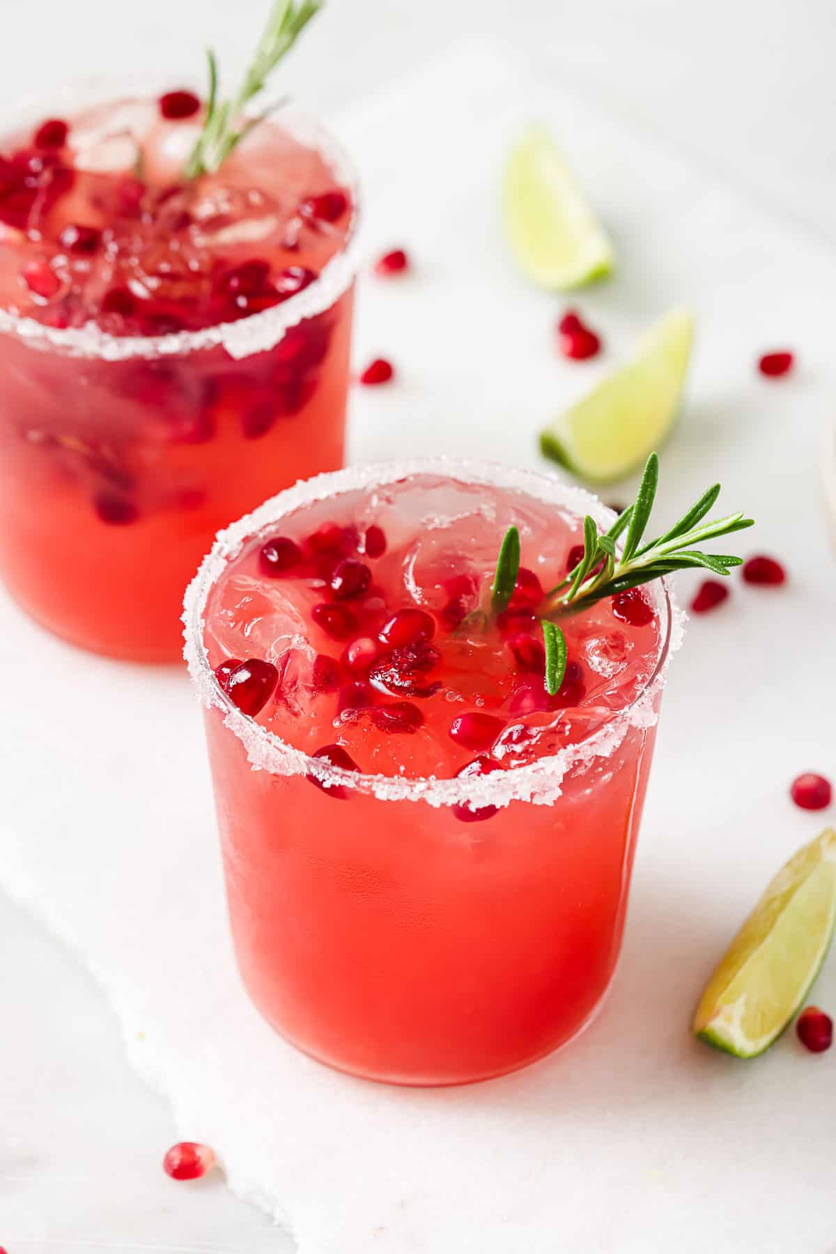 Angled photo of pomegranate margarita with pomegranate seeds and rosemary. 