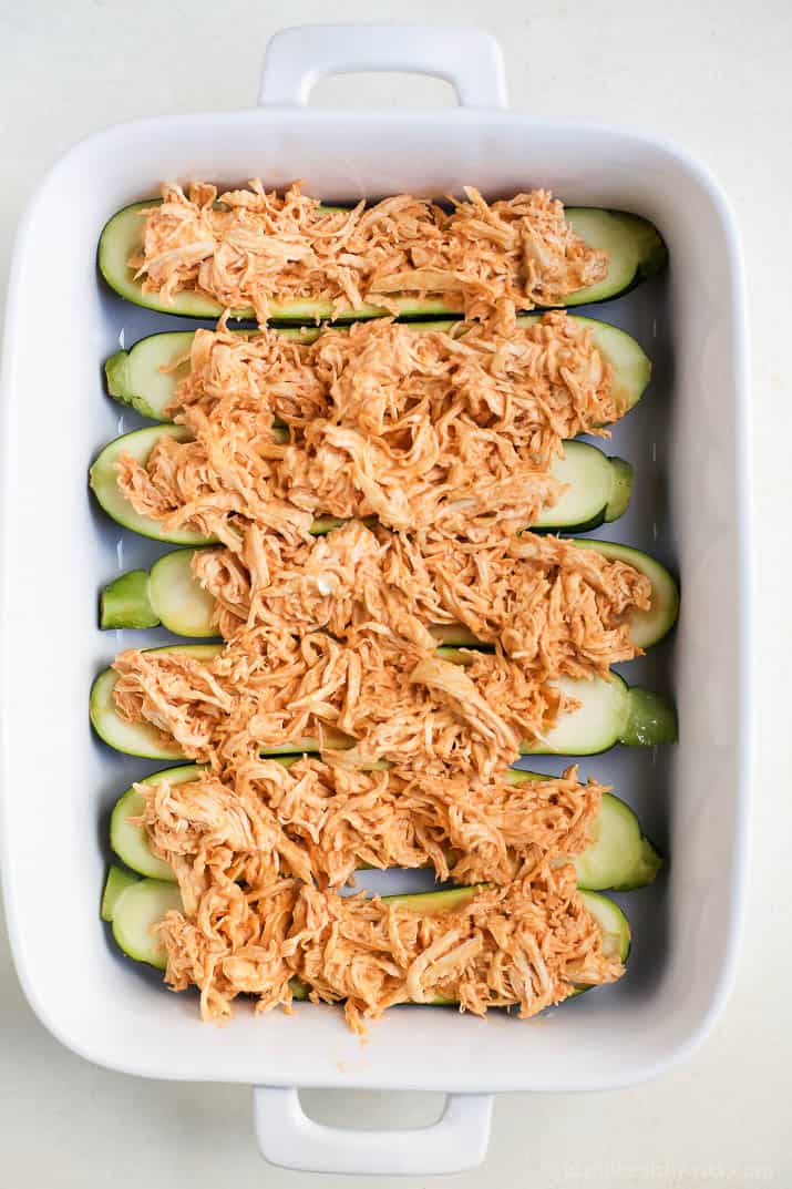 Top view of zucchini boats filled with shredded buffalo chicken in a baking dish