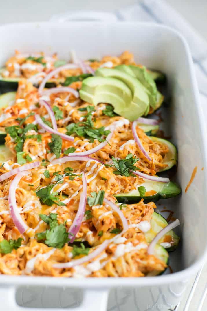 Buffalo Chicken Enchilada Zucchini Boats in a baking dish garnished with red onion slices, avocado slices and fresh cilantro