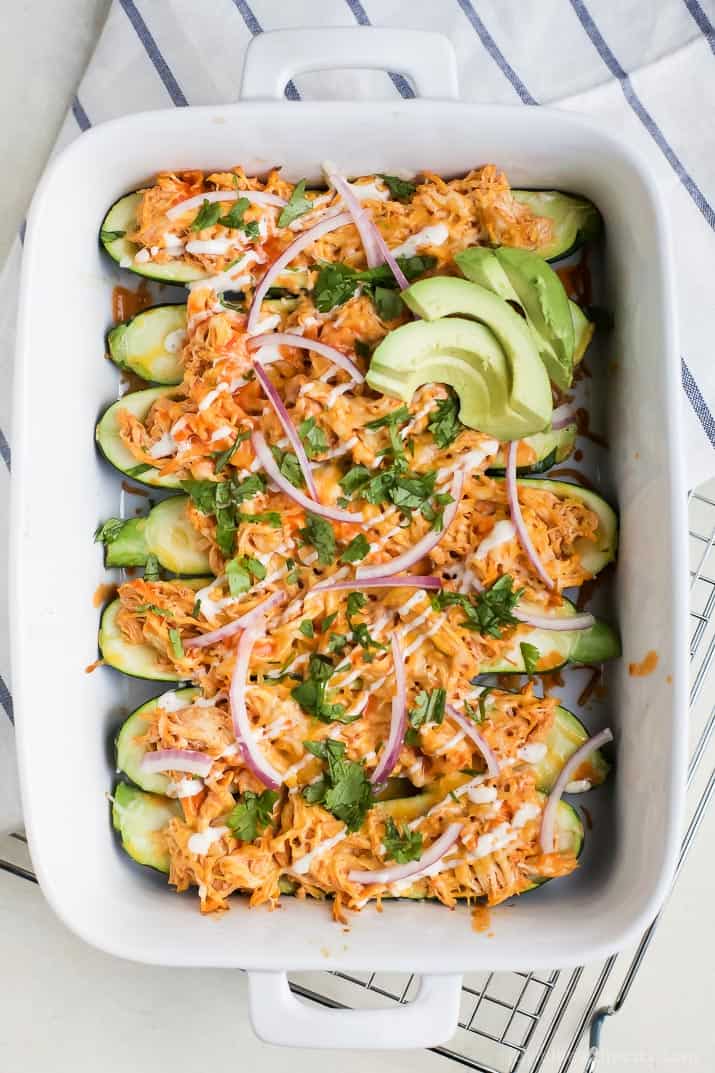 Buffalo Chicken Enchilada Zucchini Boats in a baking dish topped with avocado, red onion and fresh cilantro