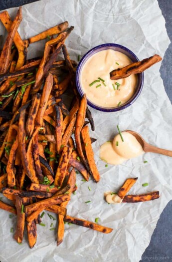 Crispy baked sweet potato fries on a sheet of parchment paper with a small bottle of honey sriracha sauce