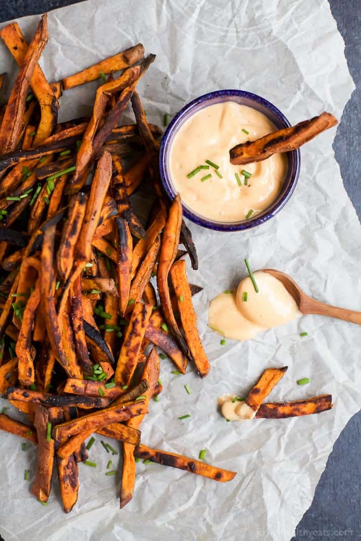 Crispy baked sweet potato fries on a sheet of parchment paper with a small bottle of honey sriracha sauce.