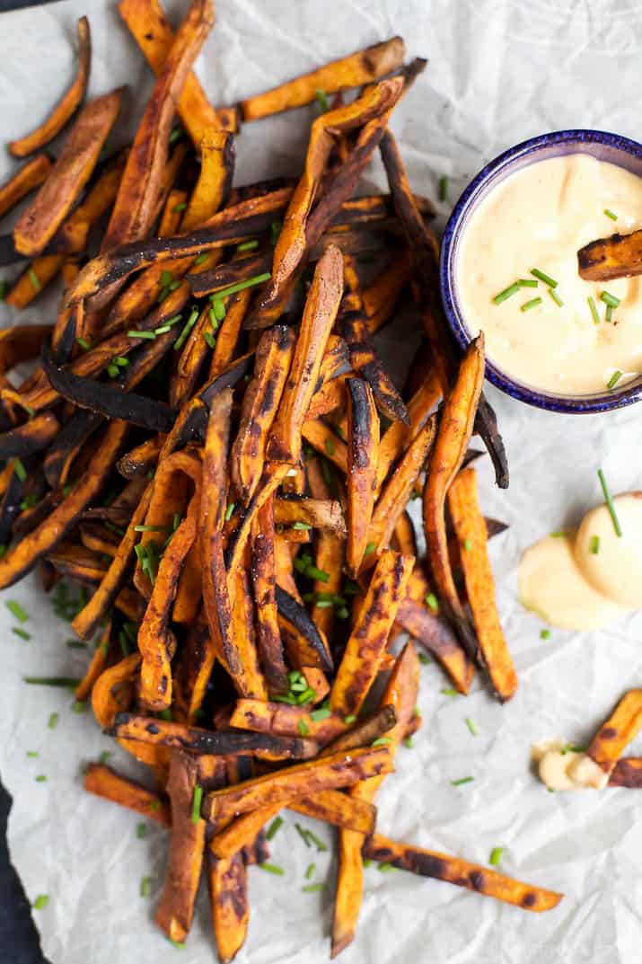 Top view of Chipotle Sweet Potato Fries with a cup of Honey Sriracha Aioli on parchment paper