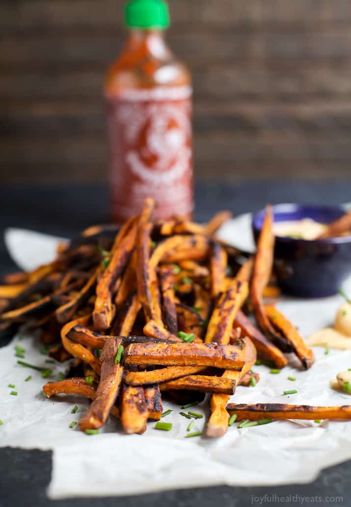 A pile of chipotle baked french fries with a bottle of sriracha in the background.