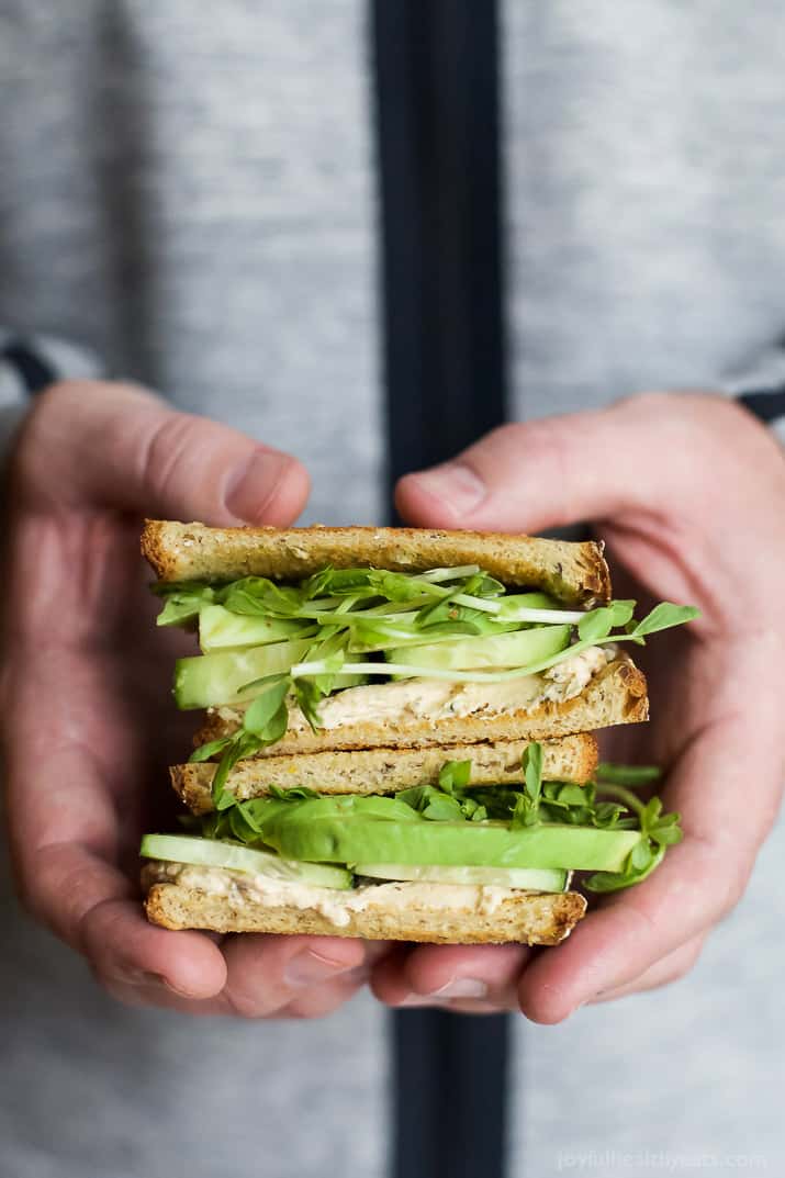 Two halves of Cucumber Avocado Sandwich stacked in a person's hands