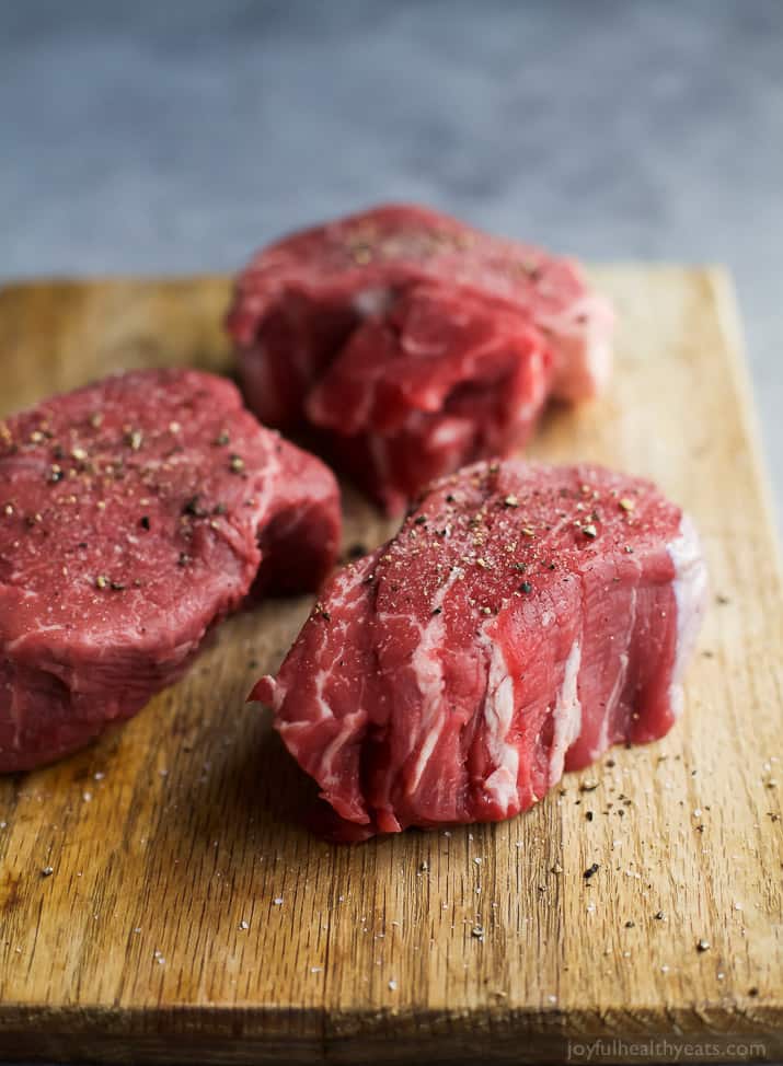 Raw filet mignon with seasonings on a wooden board