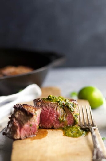 a cooked filet mignon with green sauce on a cutting board