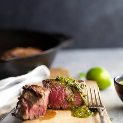 a cooked filet mignon with green sauce on a cutting board