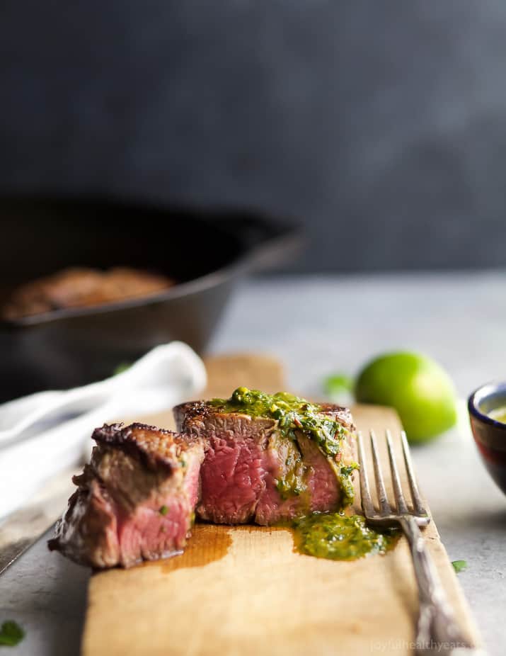 a cooked filet mignon with green sauce on a cutting board